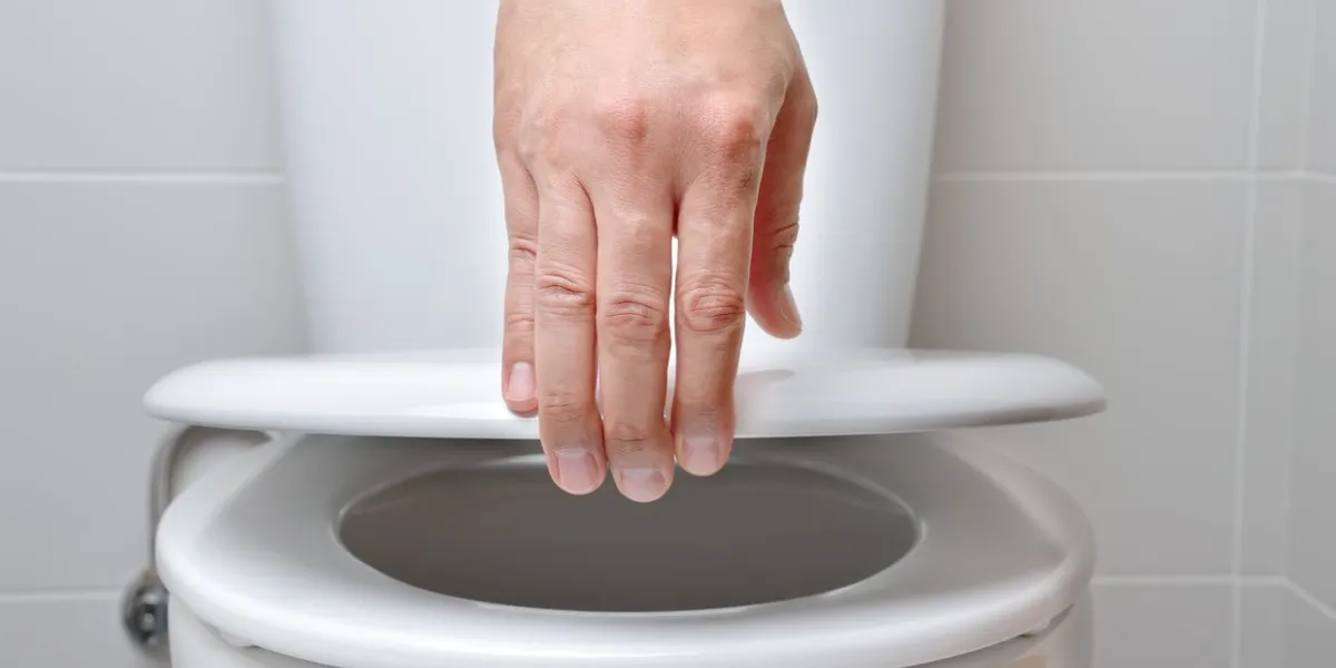 hand of a man closing the lid of a toilet