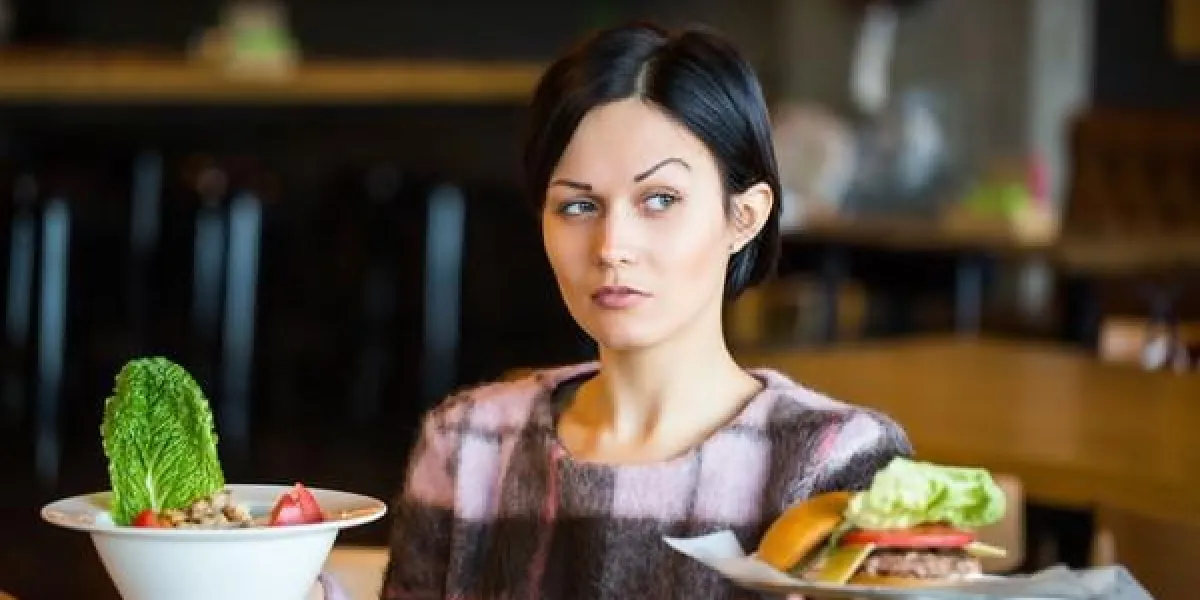 femme tenant une salade et une burgerwoman choisir entre manger sainement et malsain