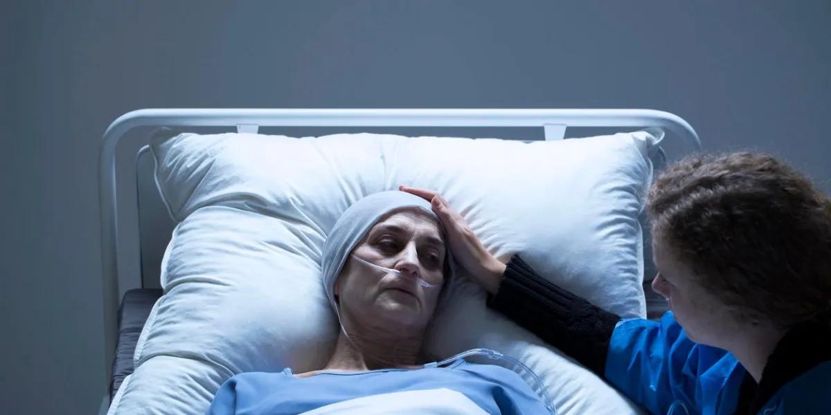 young girl helping ill, lying in bed woman in palliative ward