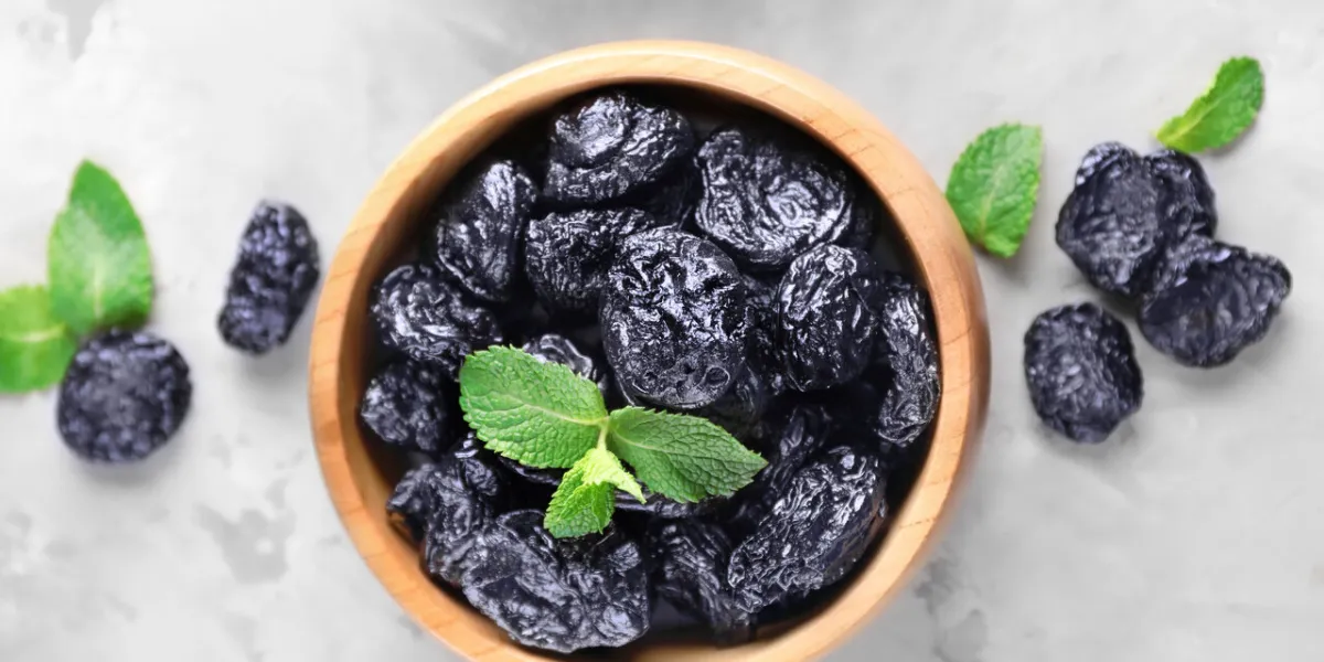 bowl with tasty dried plums on table