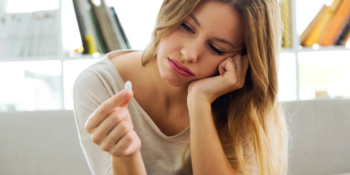 portrait of depressed young woman taking pills at home