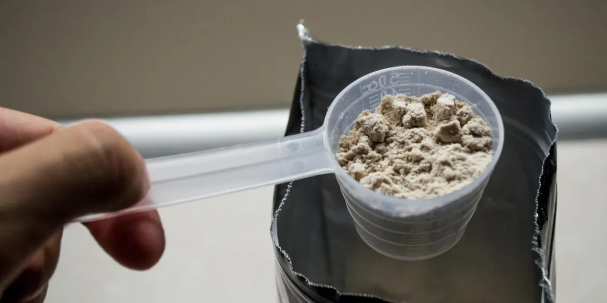 une pelle de mesure étant utilisée pour mesurer la poudre de protéine, une main mâle est visible