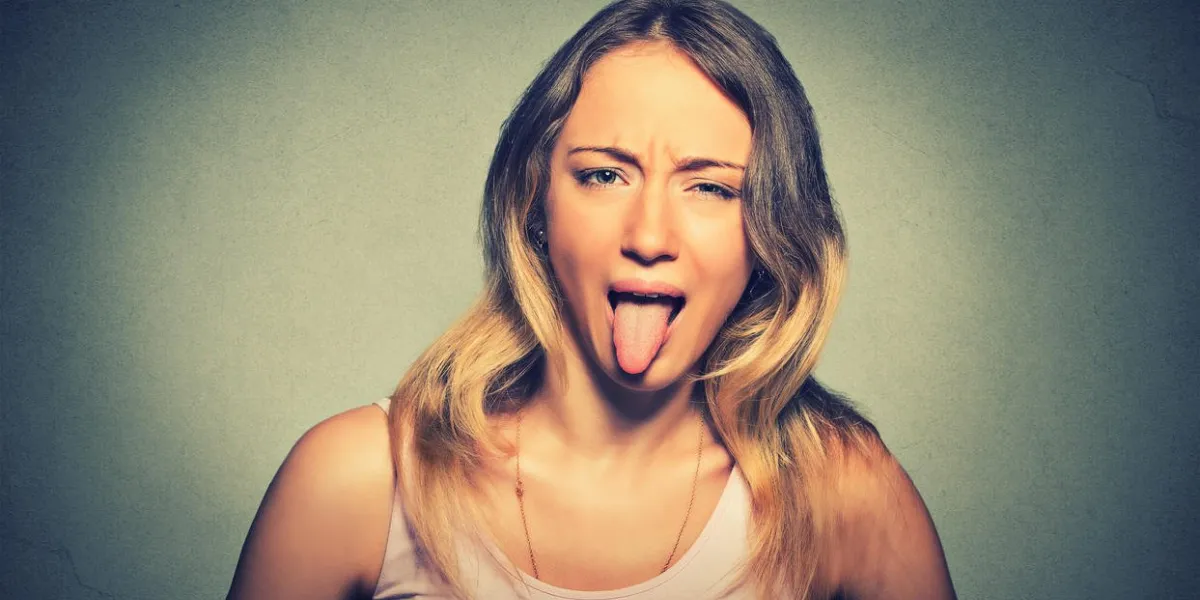 femme drôle, montrant sa langue isolée sur fond de mur gris