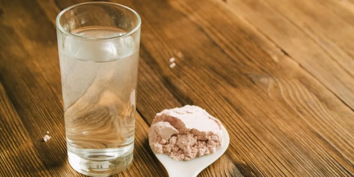 protéine de sport sur la cuillère et un verre d'eau sur la table en bois