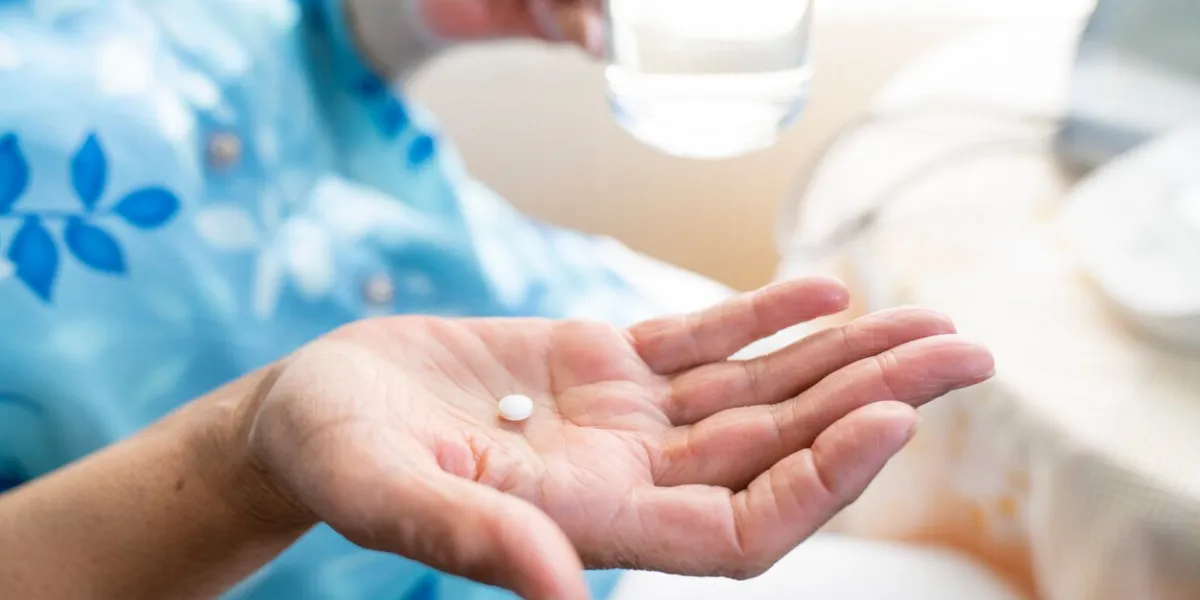 senior woman feeling sick, taking medicines in hand with a glass of water at home elderly and healthcare concept