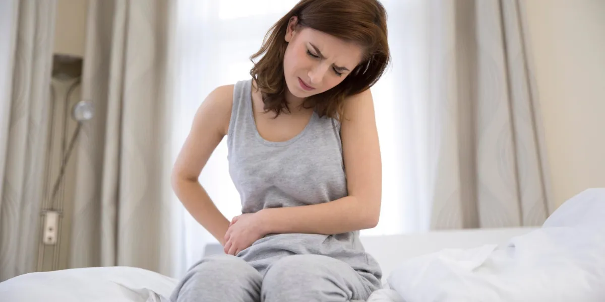 jeune femme assise sur le lit avec douleur dans l'estomac