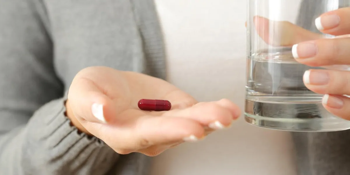 front view close up of a woman hand palm holding a capsule and a glass of water