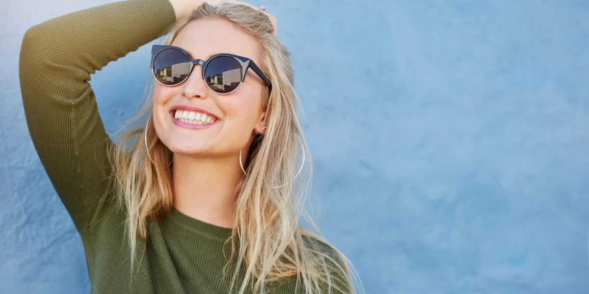 close up shot of stylish young woman in sunglasses smiling against blue background beautiful female model with copy space