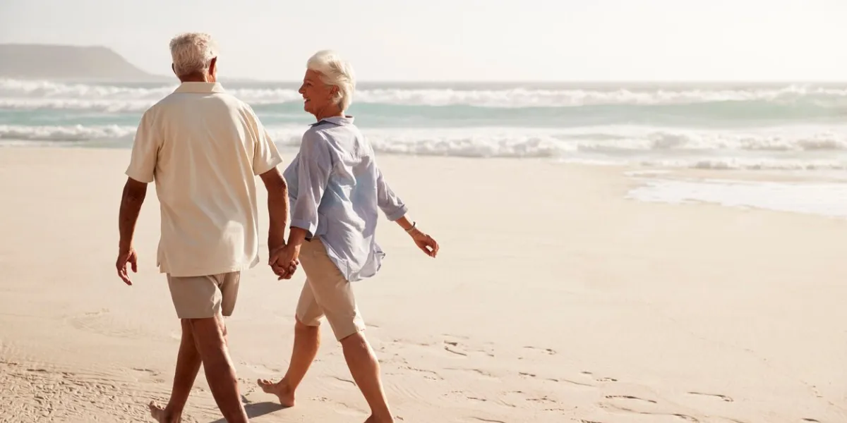 rear view of senior couple walking along beach hand in hand