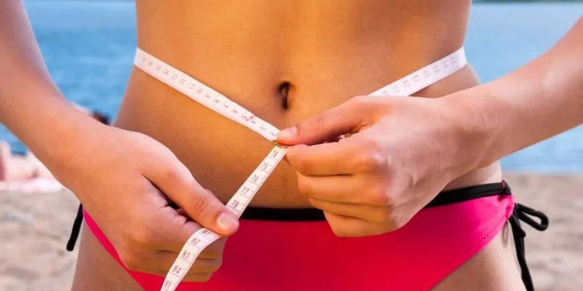 girl in swimsuit measures waist with centimeter