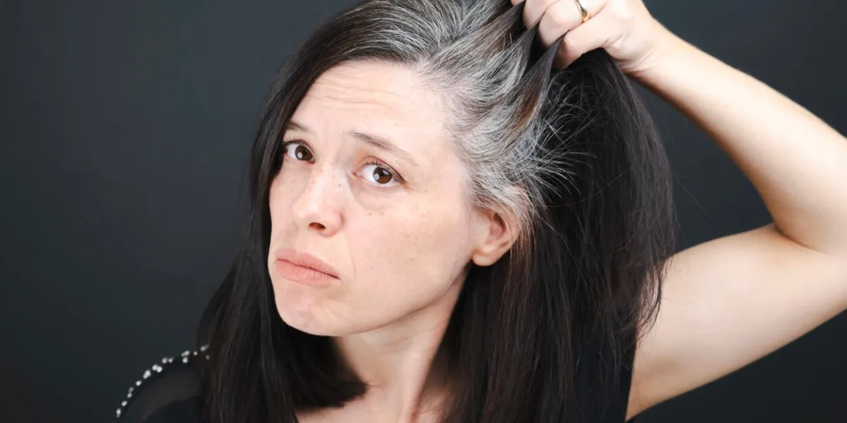 a young woman examines the gray hair on her head in a mirror on a black background close up texture of gray hair
