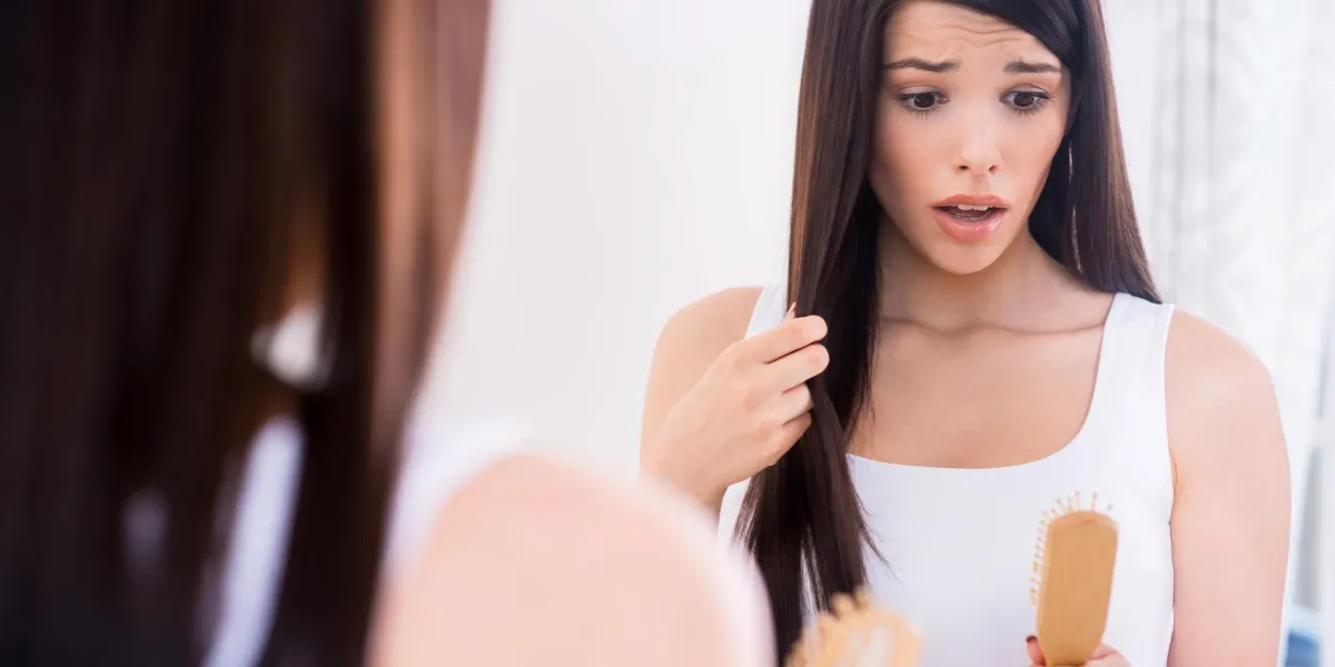 perte de cheveux déprimé jeune femme regardant sa brosse à cheveux et exprimant la négativité tout en se tenant debout contre un miroir