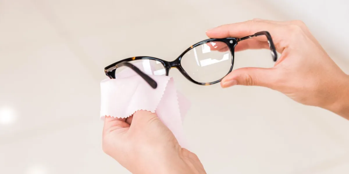 vision problems closeup hands of a woman wiping her glasses