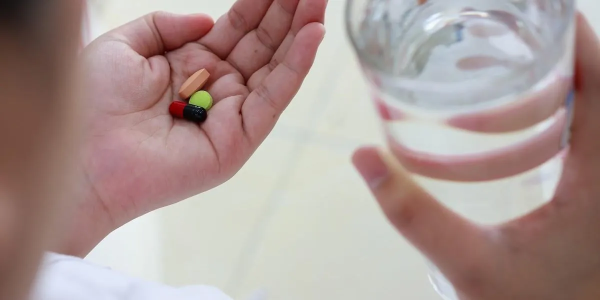 woman hands holding pills and water glass, taking medicine pills