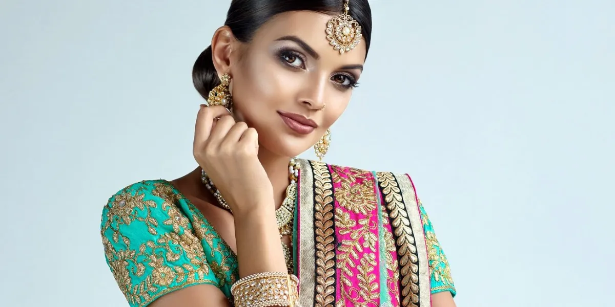 young attractive woman, dressed in a traditional indian suit-sari, with green blouse and shawl (dupatta) with gilded hand-made decoration posh jewelry set is consisting of big earrings, bright necklace, head adornment (tikka) and gold nose ring