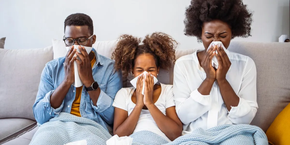 beautiful young parents and their daughter are having common cold, wiping noses and looking at camera while lying on bed sick family on bed