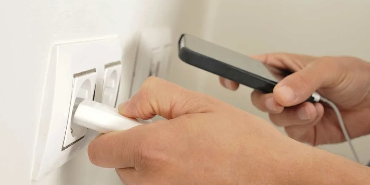 closeup of the hands of a man plugging in the plug of his smpartphone in a socket