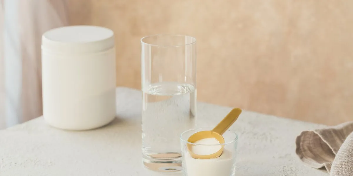 collagen powder in bowl, glass of water and measure spoon on a white wooden background extra protein intake natural beauty and health supplement concept