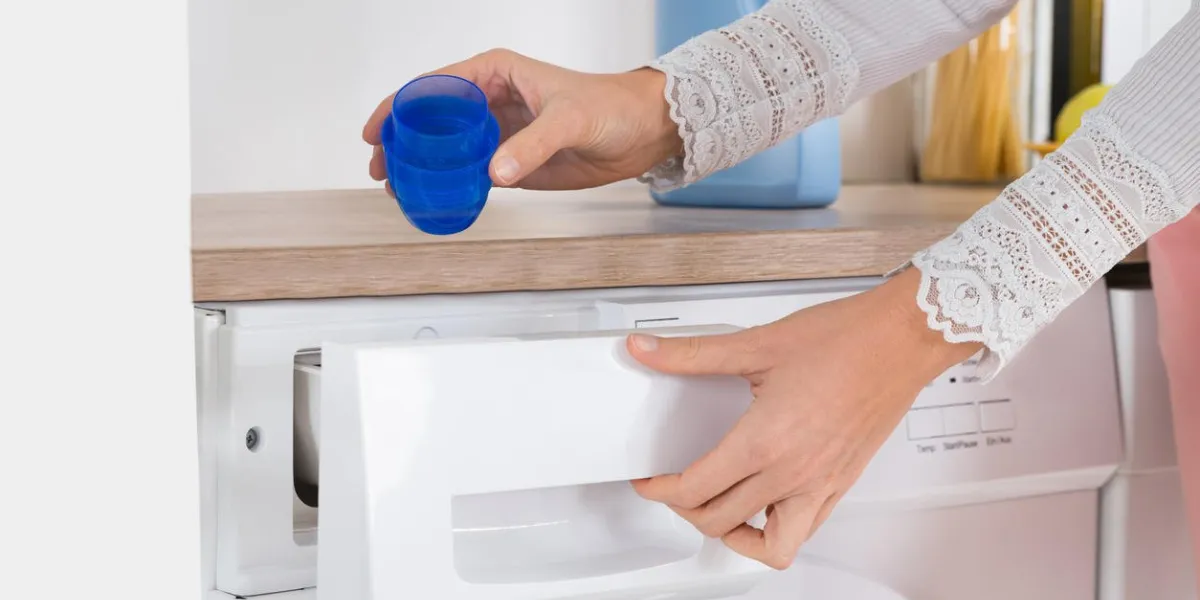 gros plan de mains féminines verser le détergent liquide dans la machine à laver à la maison