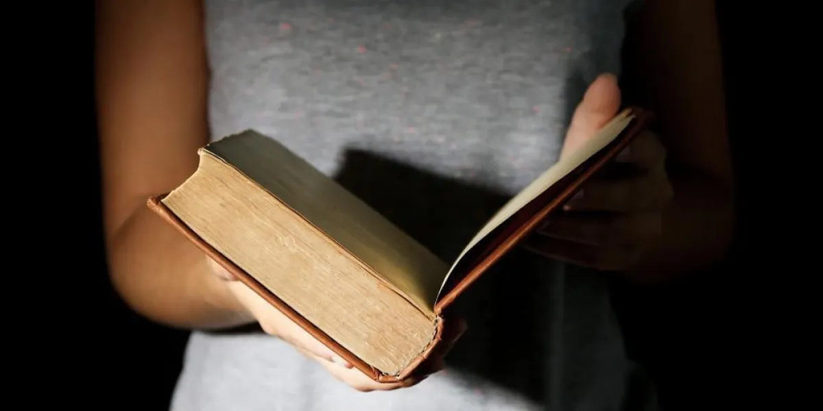 femme tenant un livre très vieux avec de la poussière, sur fond sombre