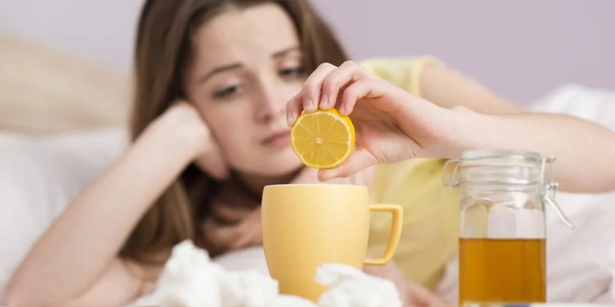 femme malade couchée dans son lit avec une forte fièvre elle a le rhume et la grippe elle boit du thé avec du miel et du citron