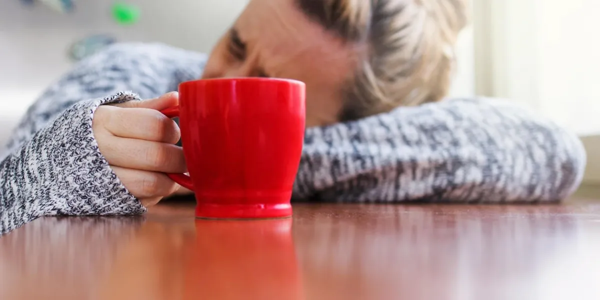 depressed woman laying on a desk with a cup of coffee in hand