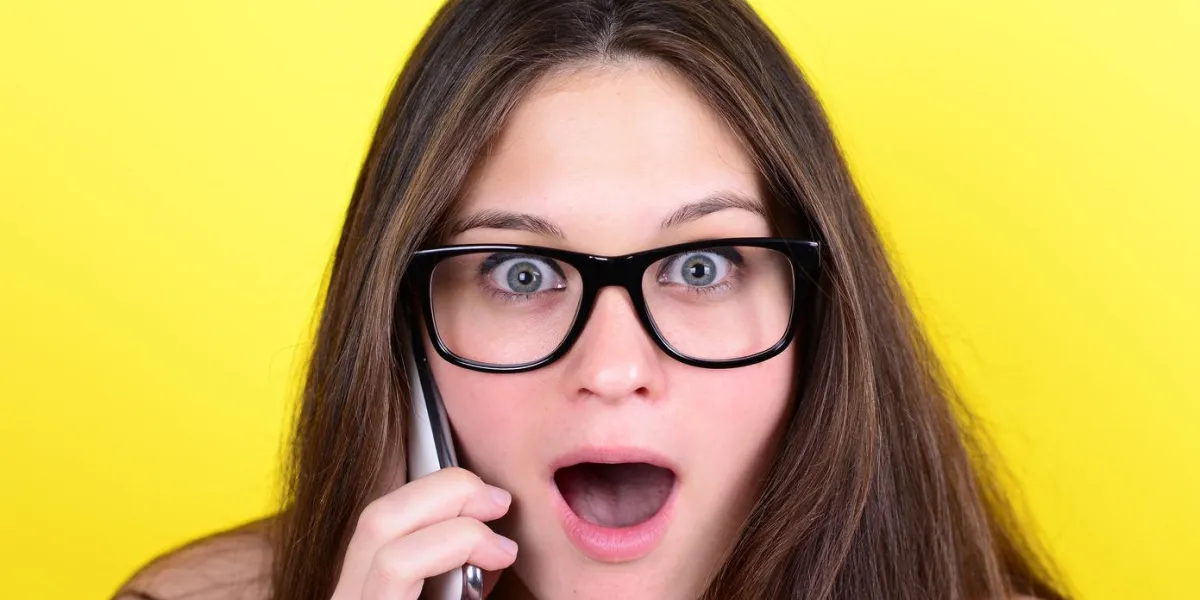 portrait de jeune femme en état de choc tout en parlant au téléphone ayant une conversation désagréable sur fond jaune
