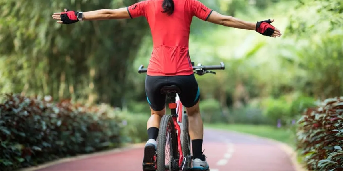 woman cyclist riding mountain bike on tropical rainforest trail with arms outstretched