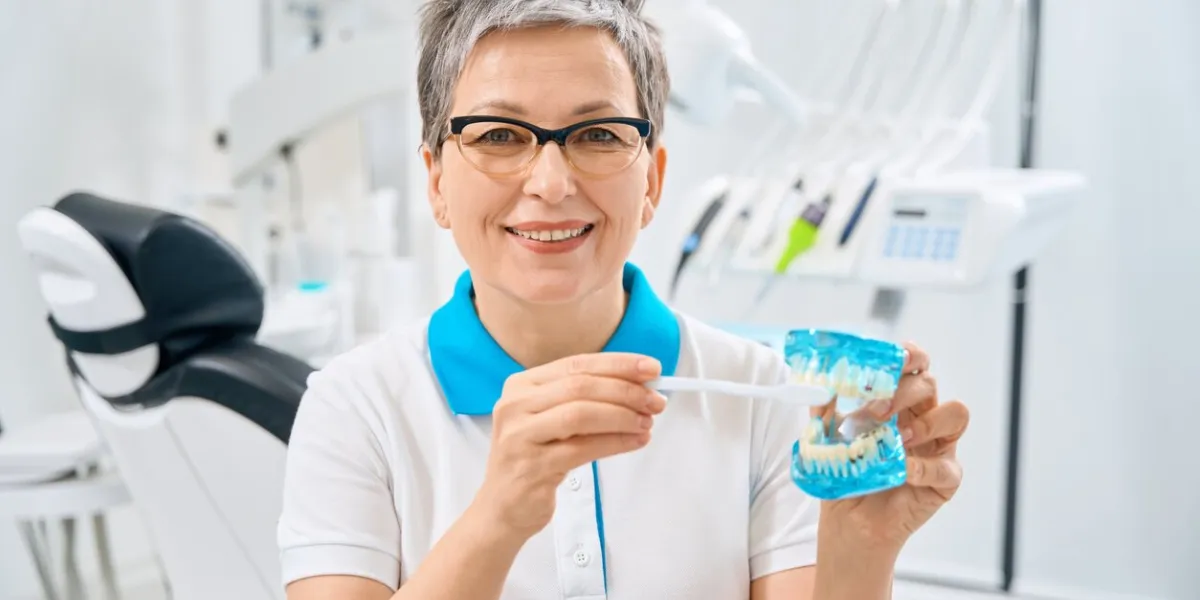 attractive adult woman dentist holding demonstrative model of jaw and toothbrush, showing how to properly clean and brush the teeth at home, professional advices, good oral hygiene