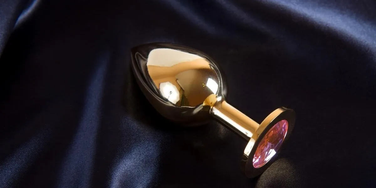 golden butt plug with pink crystal - sex toy on black background