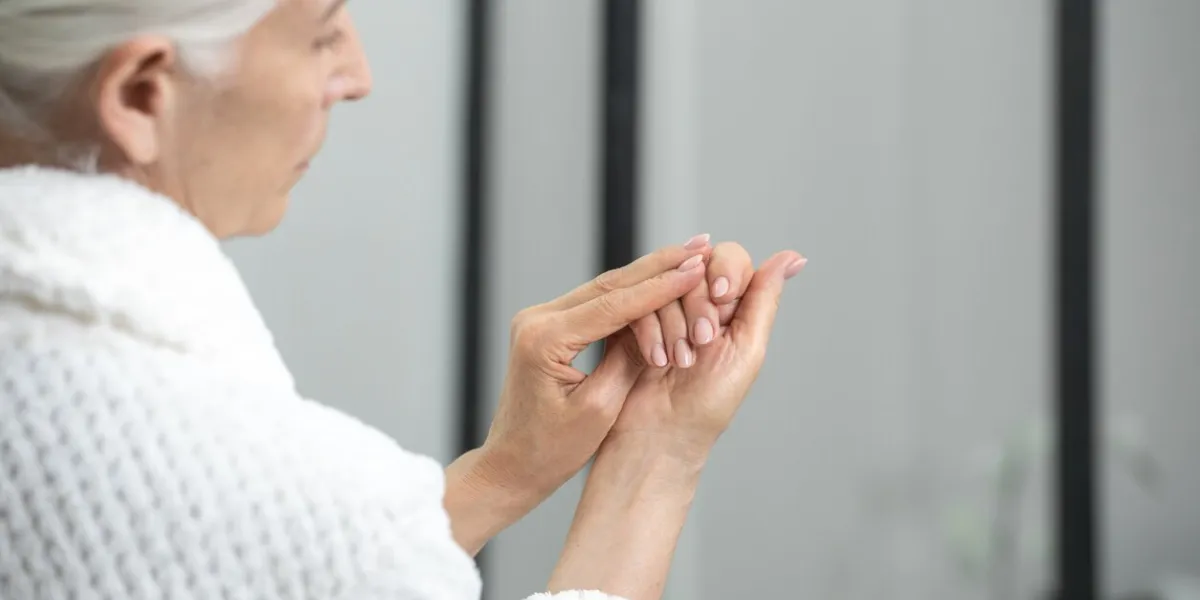 cropped view of woman in robe with gray hair looking at her nails in bathroom follow appearance concept take care of yourself idea new manicure