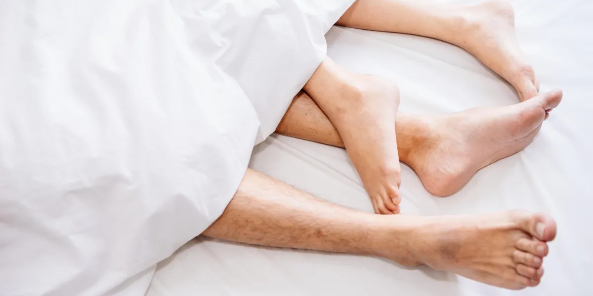 the bare foot of couples sleeping on the bed and cover by the white blanket on a bright sunday morning