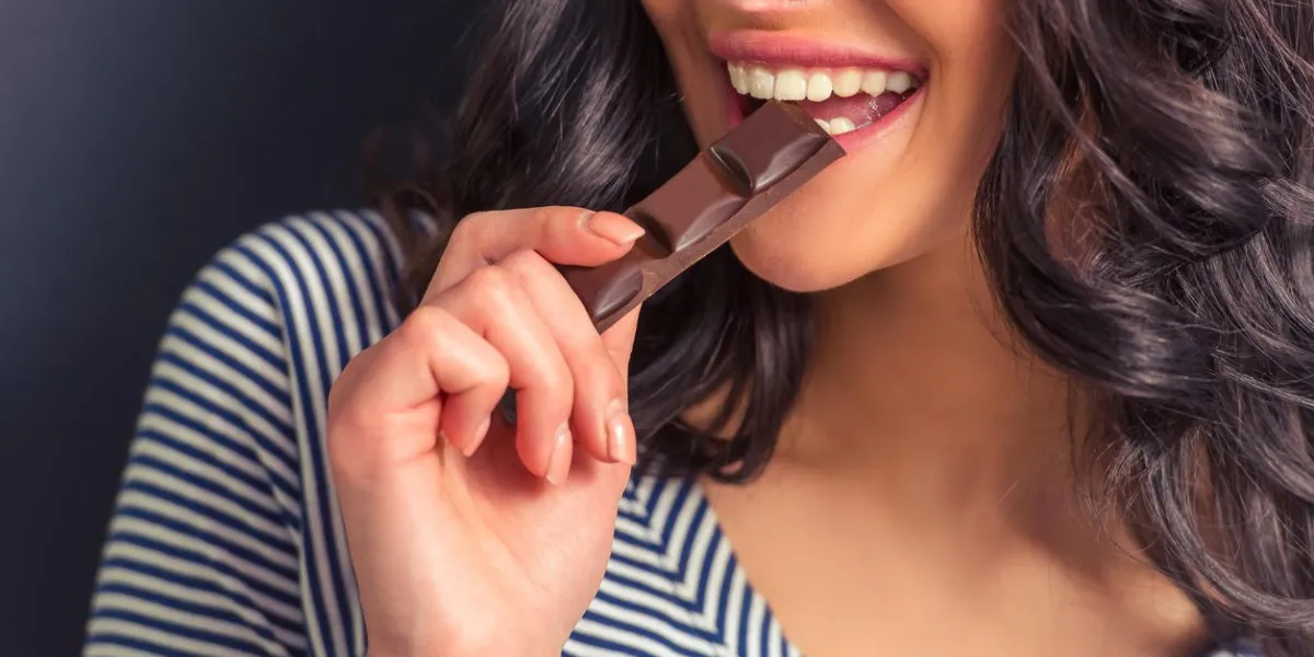 image recadrée de jolie fille mangeant chocolat et souriant, sur fond sombre