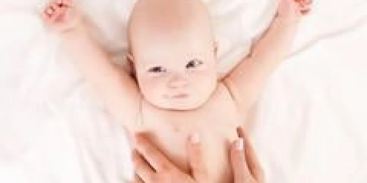 mère masser le ventre de son bébé âgé de quatre mois dans son lit à la maison, vue de dessus