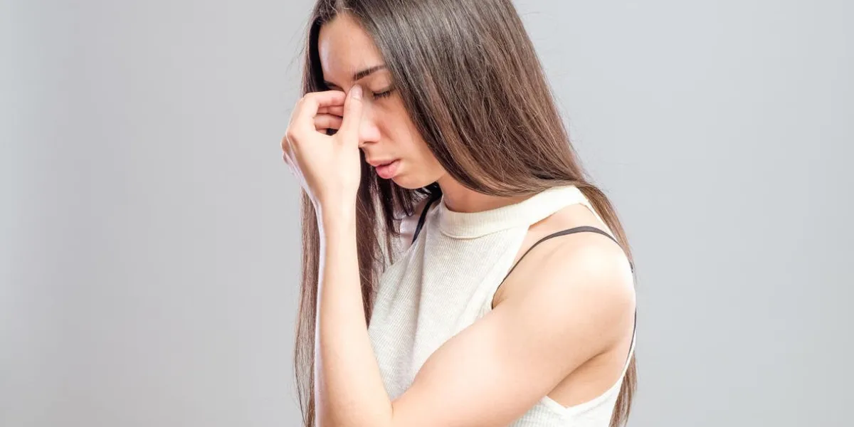 jolie jeune femme avec un mal de tête pince le pont de son nez avec une expression peinée isolée sur fond gris