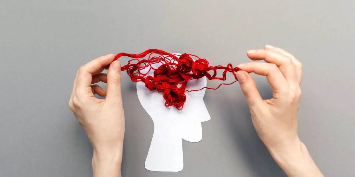 female's hands unravel the tangled red threads on the silhouette of the head, representing the brain gray background flat lay the concept of mental health and psyhology problem