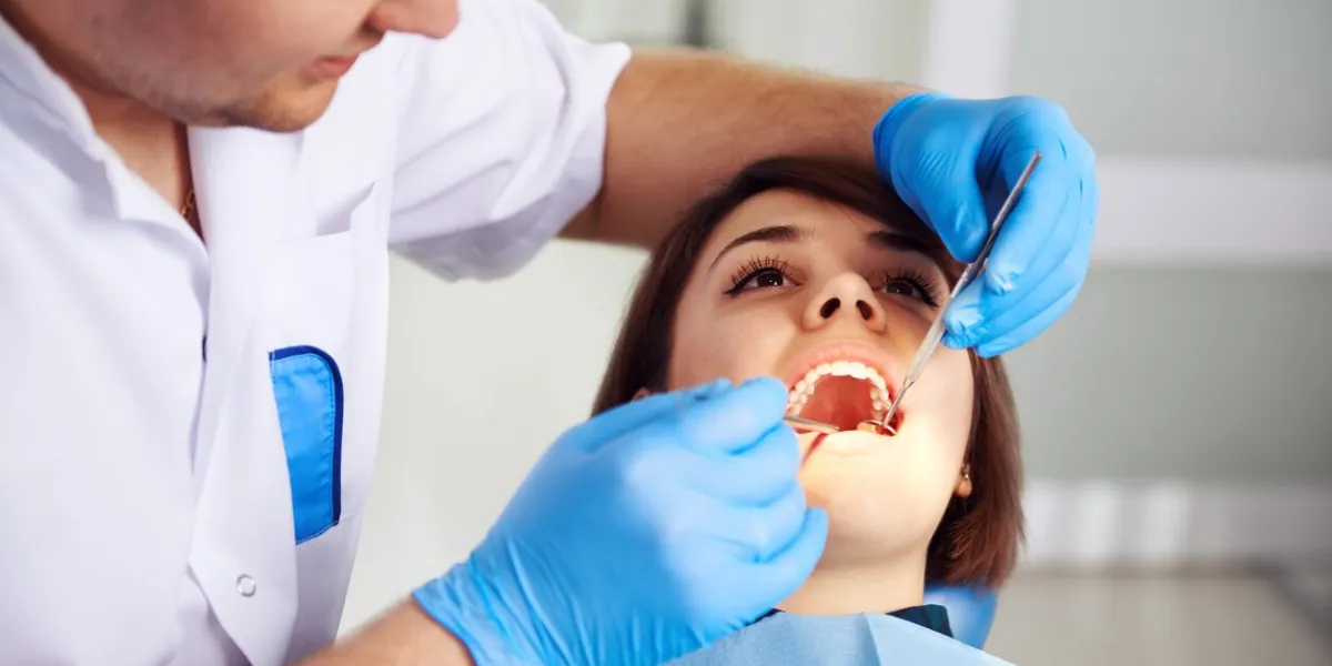 male doctor in uniform checking up female patient's teeth in dental clinic concept of oral examination, toothache and decay treatment