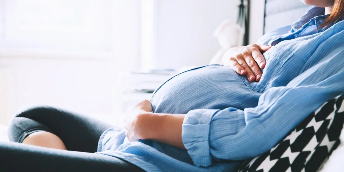 belle femme enceinte assis au lit et tient les mains sur le ventre dans la chambre à la maison grossesse, parenthood, préparation et attente concept close-up, à l'intérieur