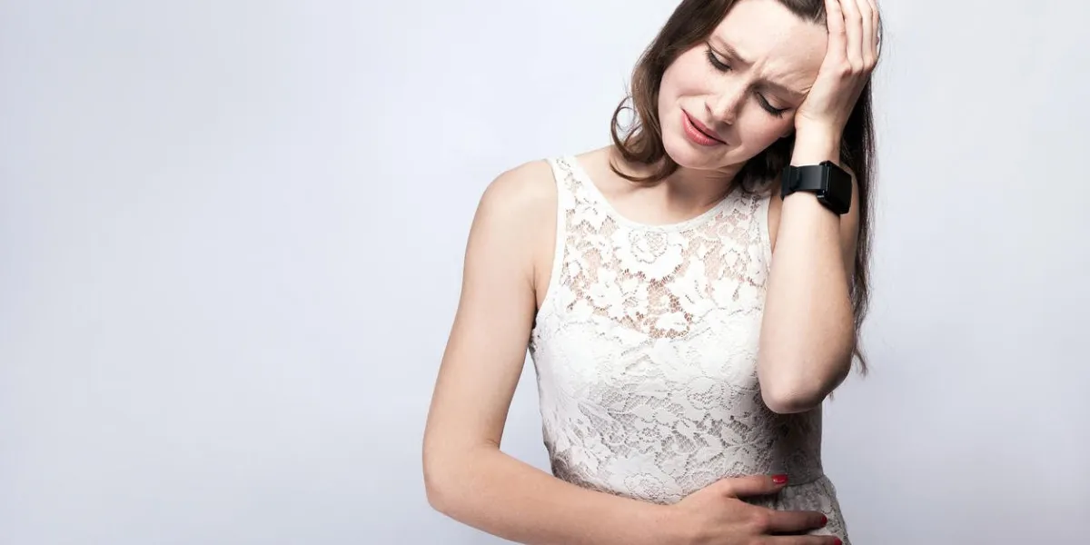 portrait of beautiful woman with freckles and white dress and smart watch with stomach pain on silver gray background healthcare and medicine concept