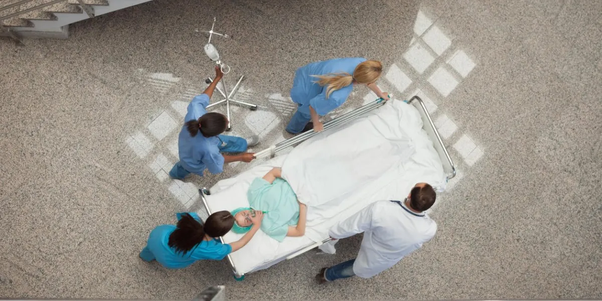 three nurses and one doctor pushing one patient in a bed in hospital corridor