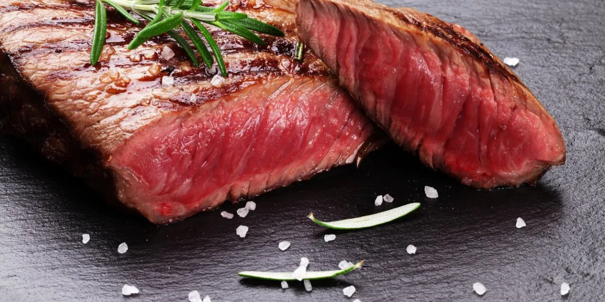 grilled beef steak with rosemary, salt and pepper on black stone plate