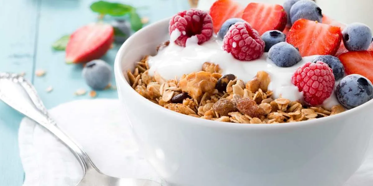 healthy breakfast in a bowl with homemade baked granola, frozen berries, fresh strawberries and yogurt on a turquoise wooden table
