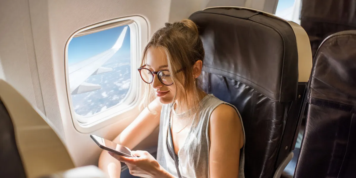 young woman sitting with phone on the aircraft seat near the window during the flight in the airplane