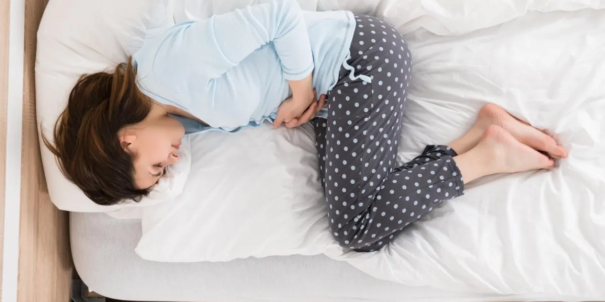 young woman with stomach ache lying on bed