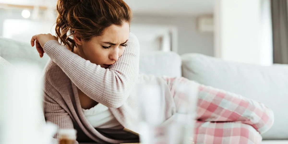 young woman coughing into elbow while lying down on sofa in the living room