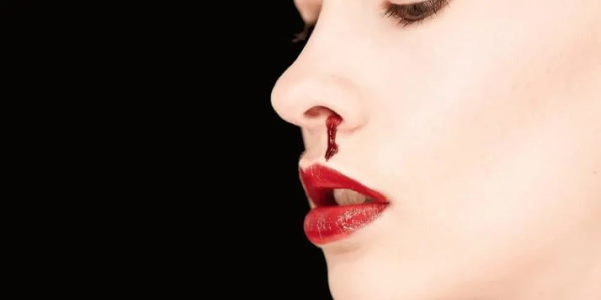 portrait d'une femme pâle portant le rouge à lèvres et un nez sanglant isolé sur un fond noir