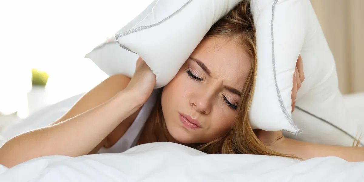belle jeune femme couchée dans son lit souffrant d'insomnie couvrant la tête et les oreilles avec oreiller et faire un visage désagréable bruyant voisin, le stress, le son de l'alarme, empêcher le concept de sommeil