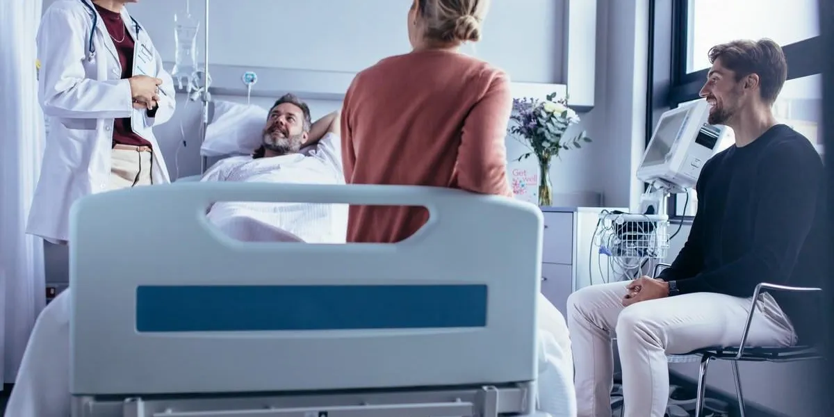 family and friends visiting patient in hospital ward and talking with doctor female physician sharing the recovery of hospitalised man with his friends