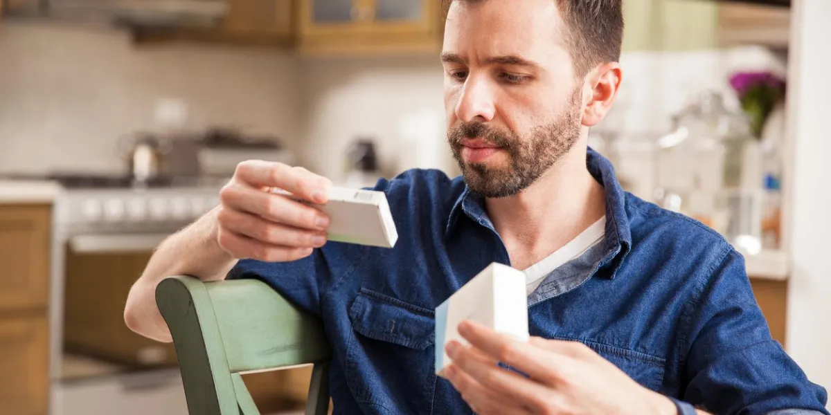 homme séduisant avec une barbe tenant un couple de boîtes de médicaments et se comparant à la maison