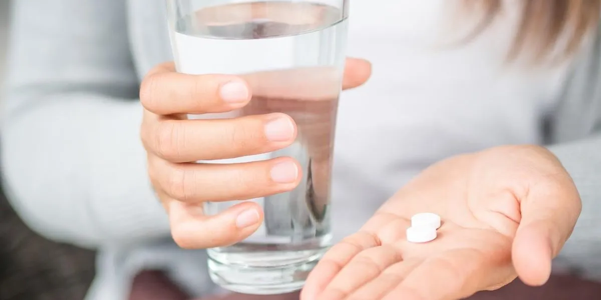 closeup woman hand with pills medicine tablets and glass of water for headache treatment healthcare, medical supplements concept
